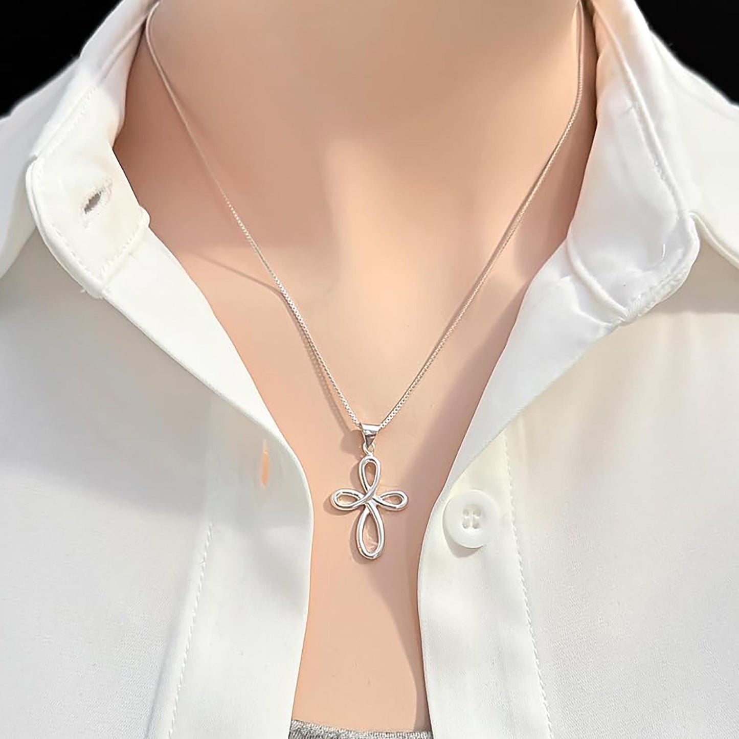 A silver cross pendant necklace is worn around a person's neck, with a white collared shirt visible underneath.