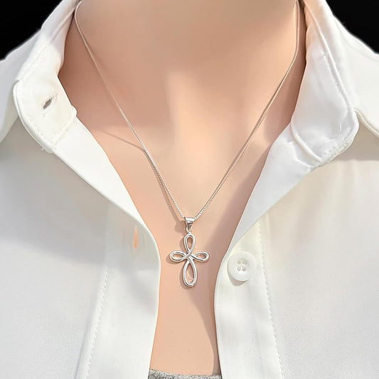 A silver cross pendant necklace is worn around a person's neck, with a white collared shirt visible underneath.