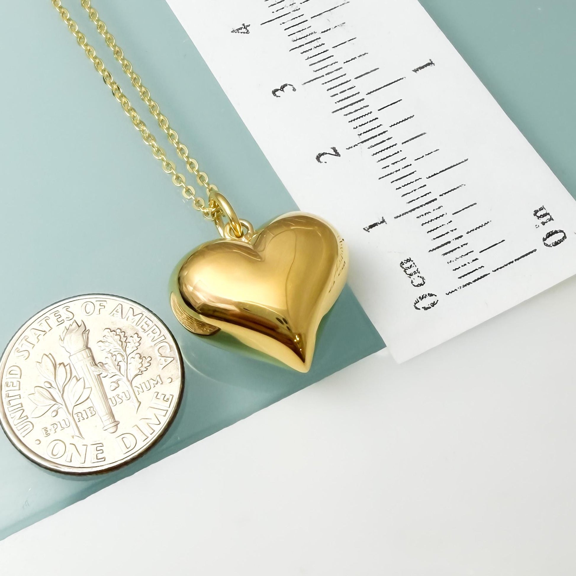 a gold heart-shaped pendant necklace and a United States one-dollar coin, with a ruler placed next to them.