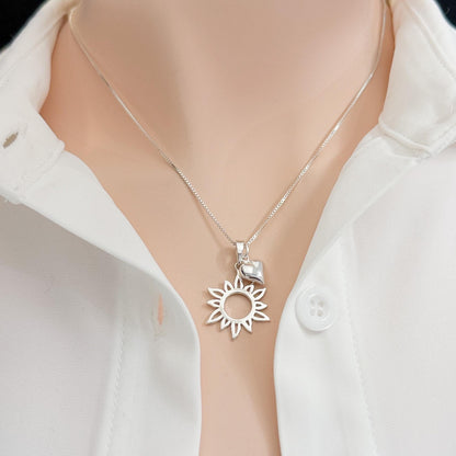A silver necklace with a pendant featuring a sun design is shown against a white shirt collar.