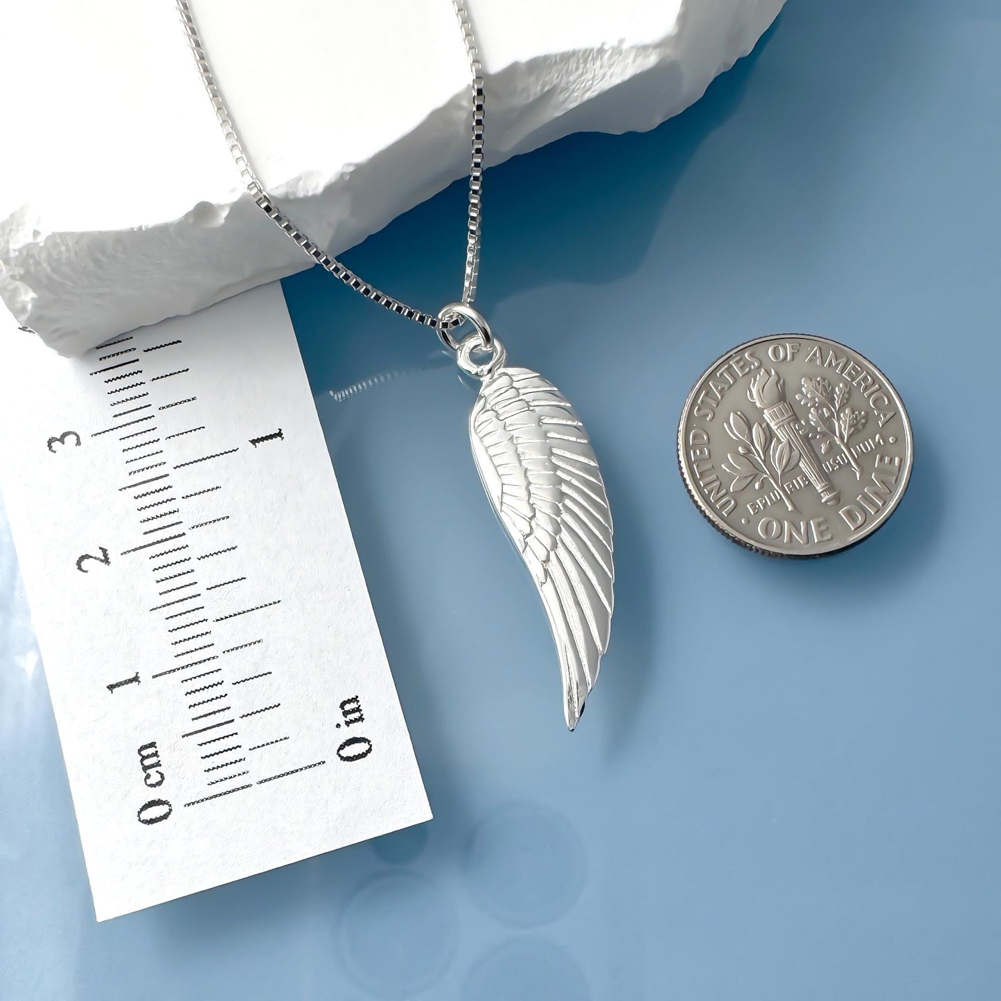 a silver wing pendant necklace and a United States quarter coin placed on a blue surface.