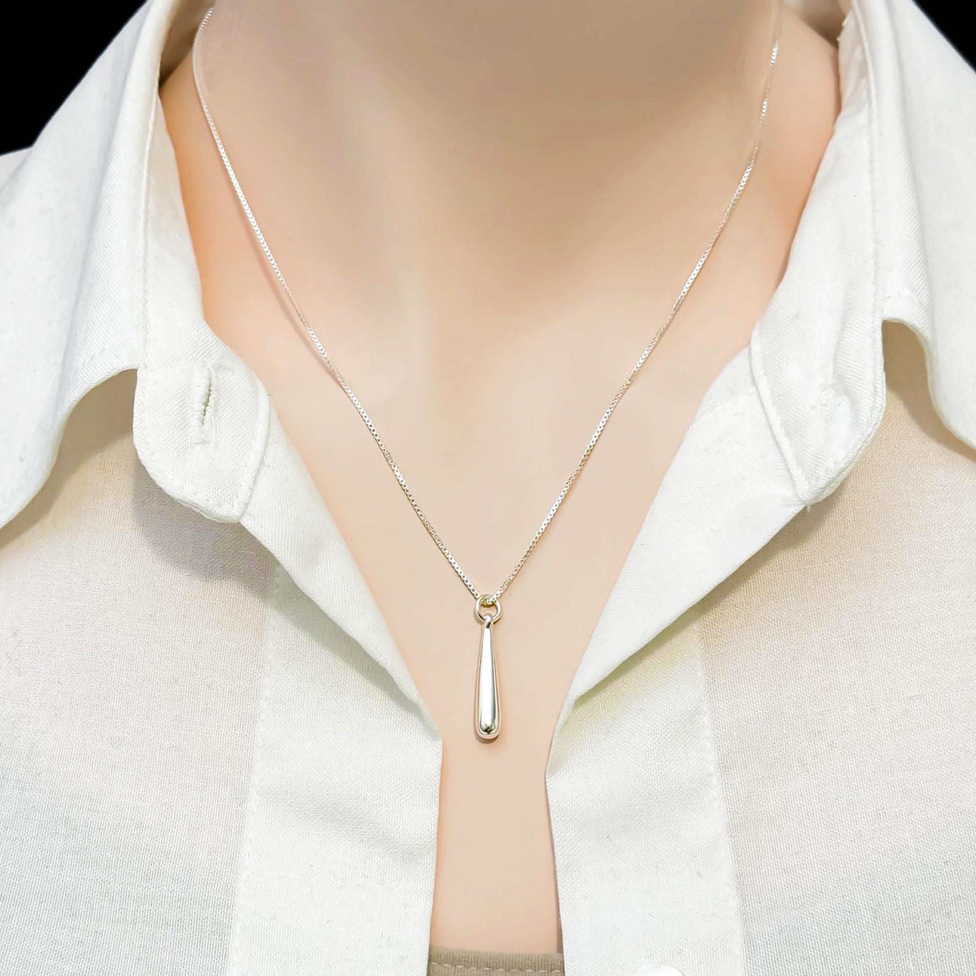 A close-up view of a person wearing a white collared shirt and a silver necklace with a pendant.