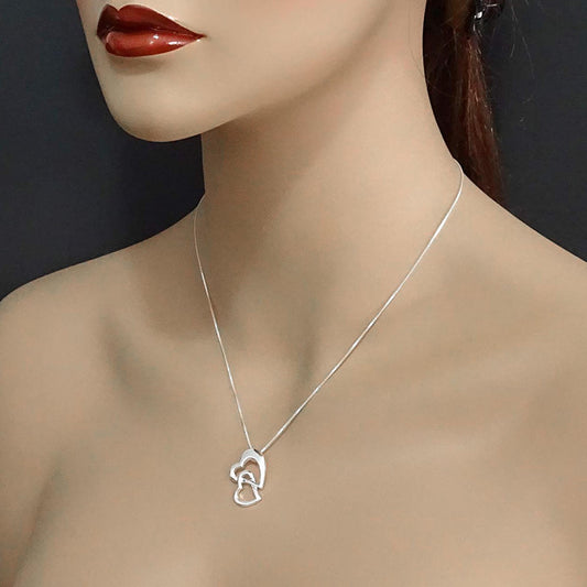 A close-up of a woman's neck and chest area wearing a silver necklace with a heart-shaped pendant.