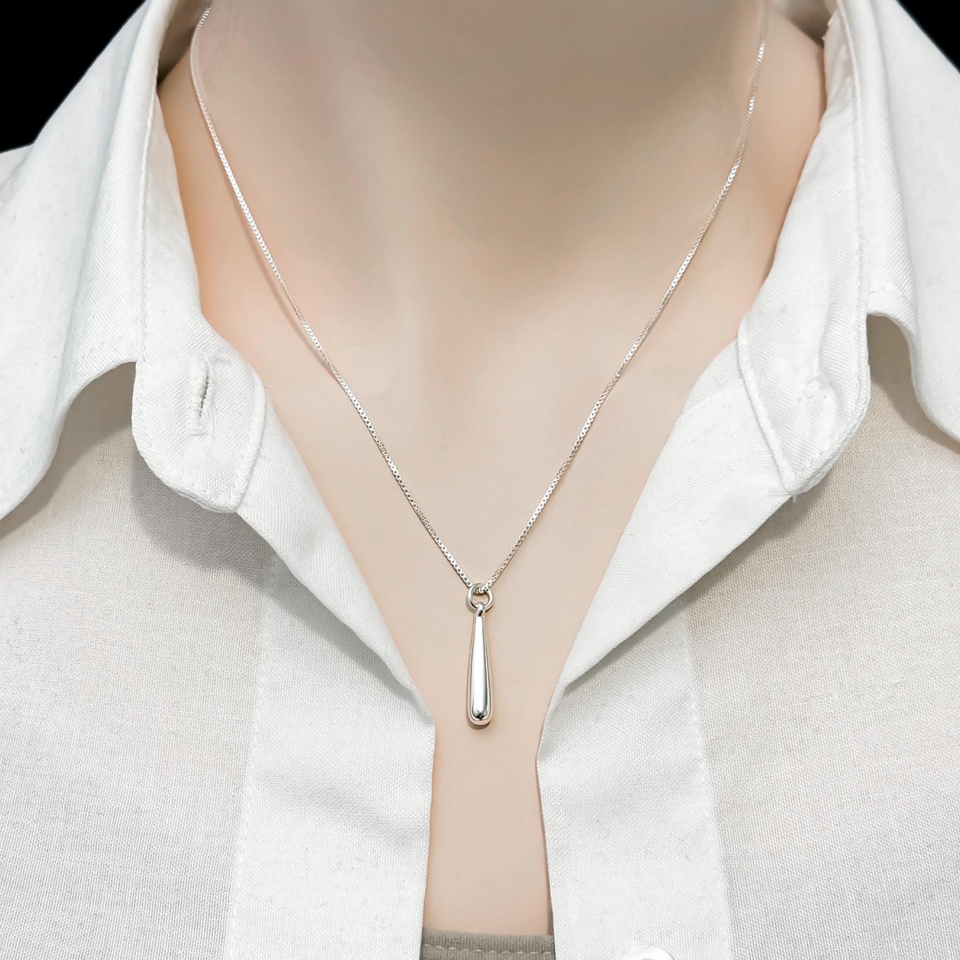 A close-up view of a silver necklace with a pendant, worn around a person's neck.