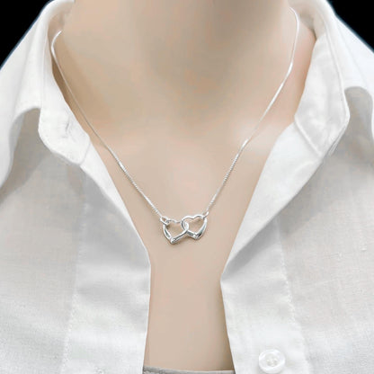 A silver necklace with a heart-shaped pendant is displayed on a person's neck.