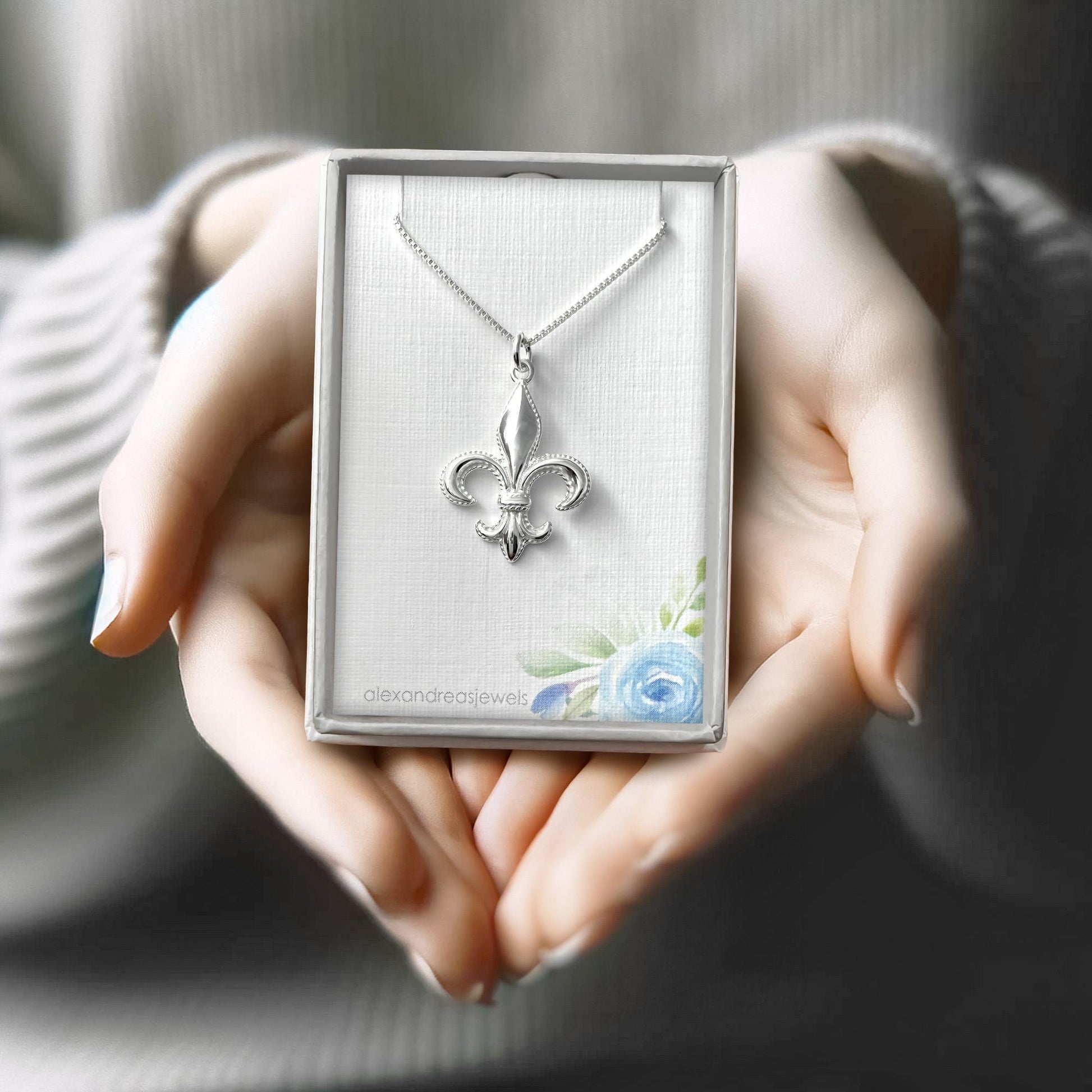 A person's hands holding a silver necklace with a pendant in a box.