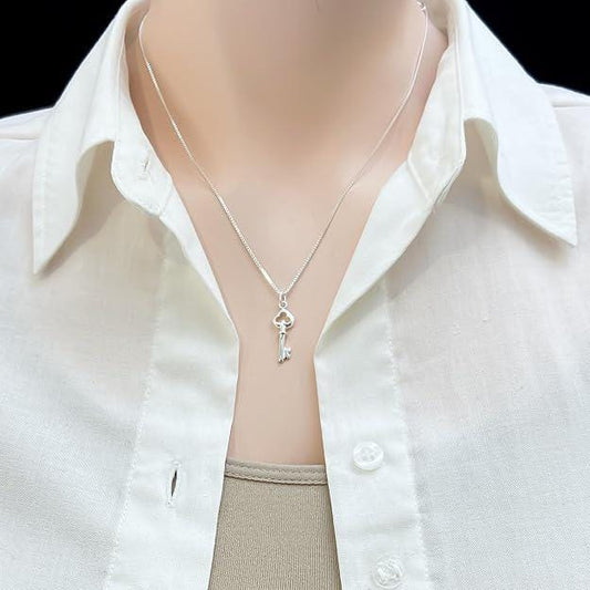 A silver necklace with a key pendant is worn around a person's neck, with a white collared shirt visible underneath.