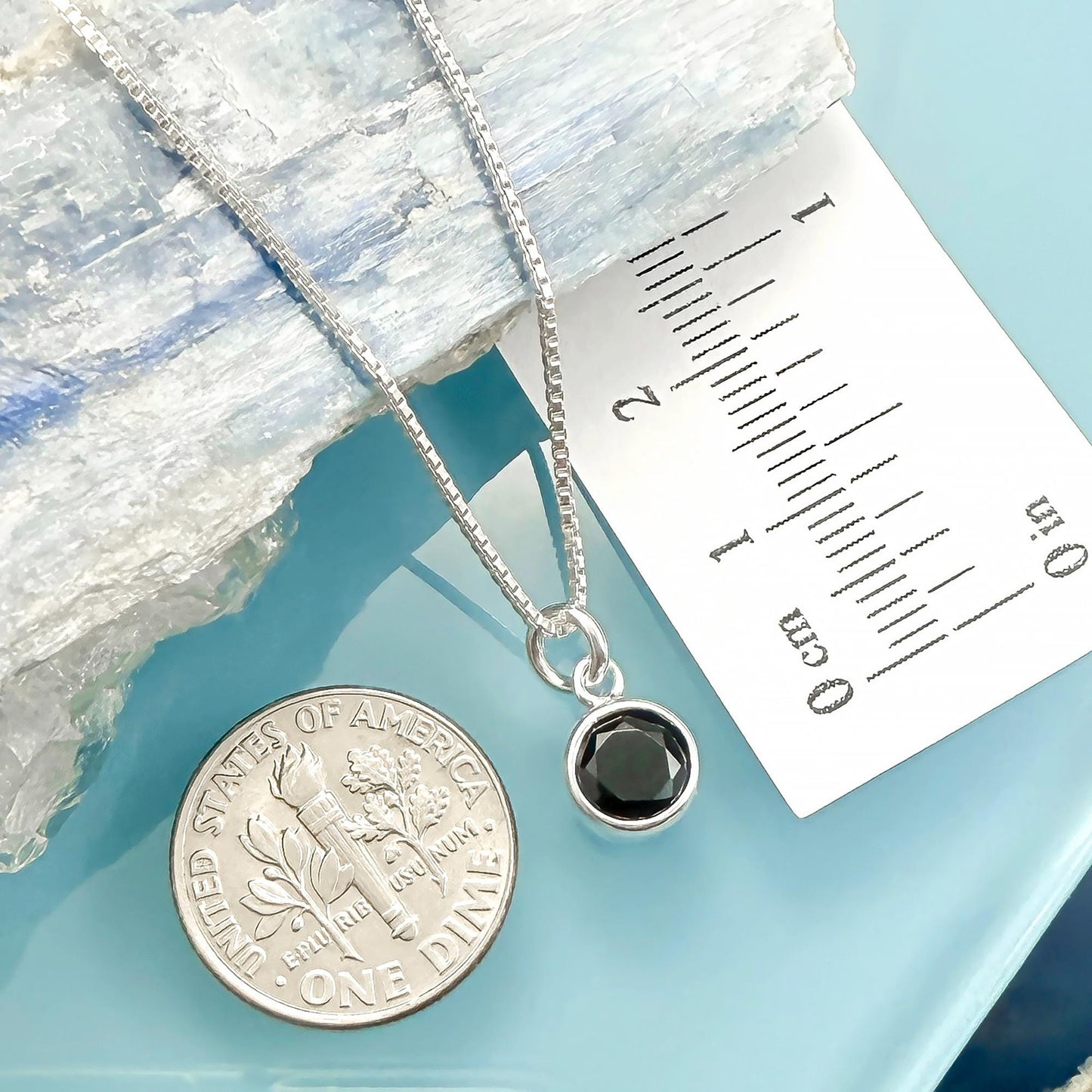 a silver necklace with a black gemstone pendant, placed next to a United States one-dollar coin.