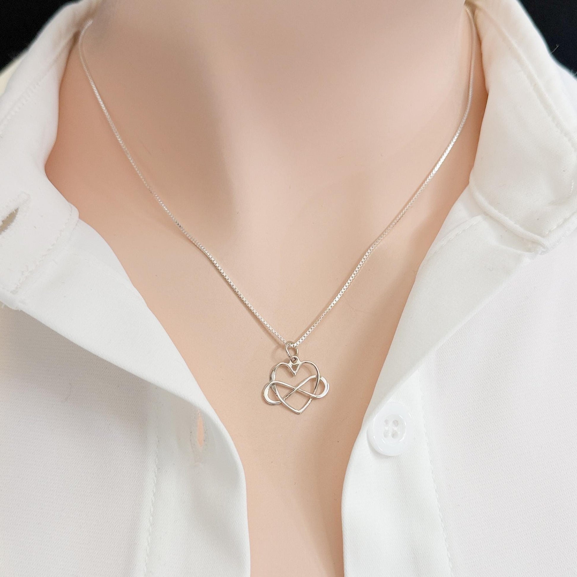 A silver necklace with a heart-shaped pendant is worn around a person's neck.