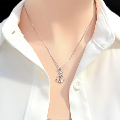 A silver necklace with a small anchor pendant is worn around a person's neck, who is wearing a white collared shirt.