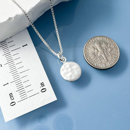 A silver necklace with a pendant is placed next to a United States one dollar coin, which is lying on a blue surface.