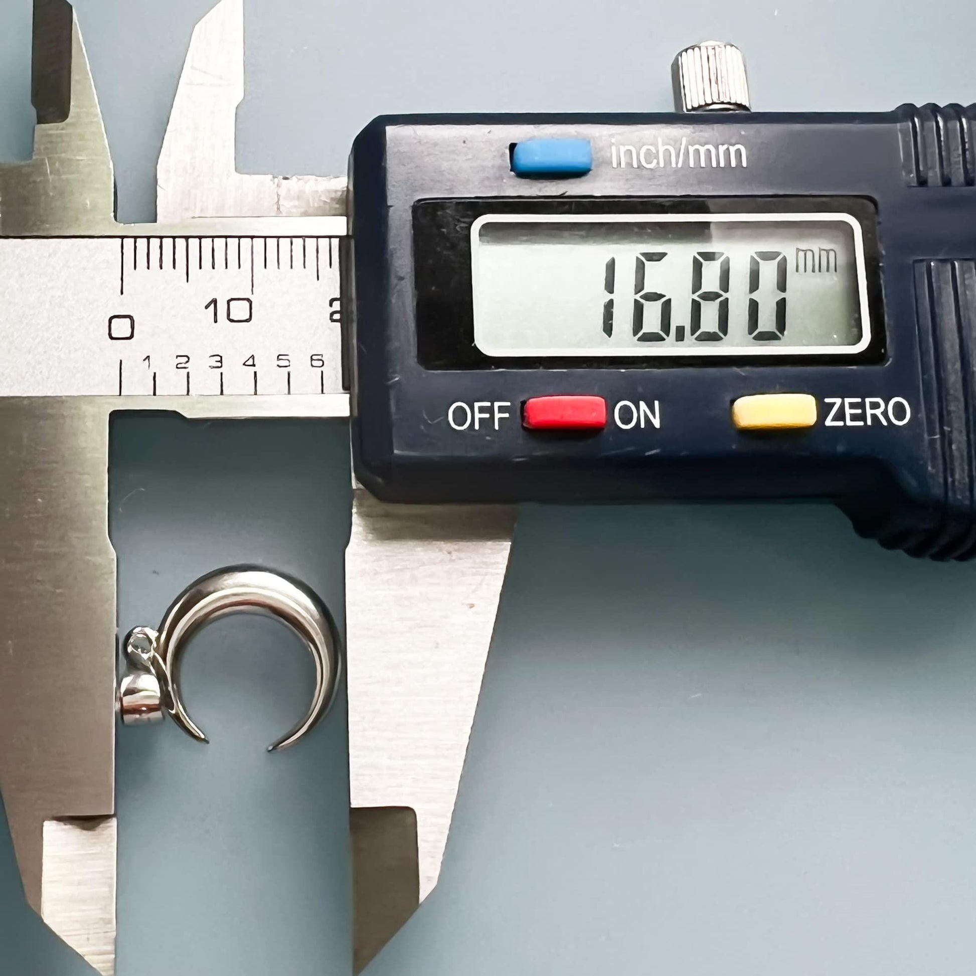 A digital caliper is being used to measure the size of a silver ring, displaying the measurement as 16.80 millimeters.