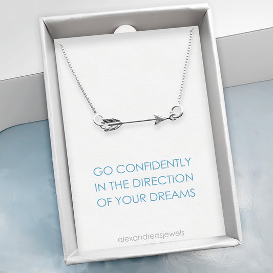 A silver necklace with an arrow pendant is displayed in a white box with a blue background.
