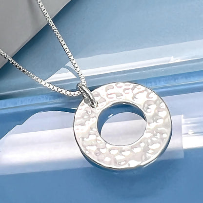 A silver necklace with a round pendant is displayed against a blue background.