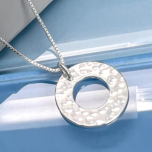 A silver necklace with a round pendant is displayed against a blue background.