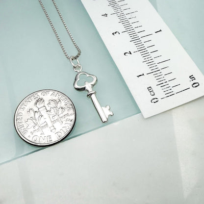 a silver key pendant and a United States one-dollar coin, both placed on a light blue surface.