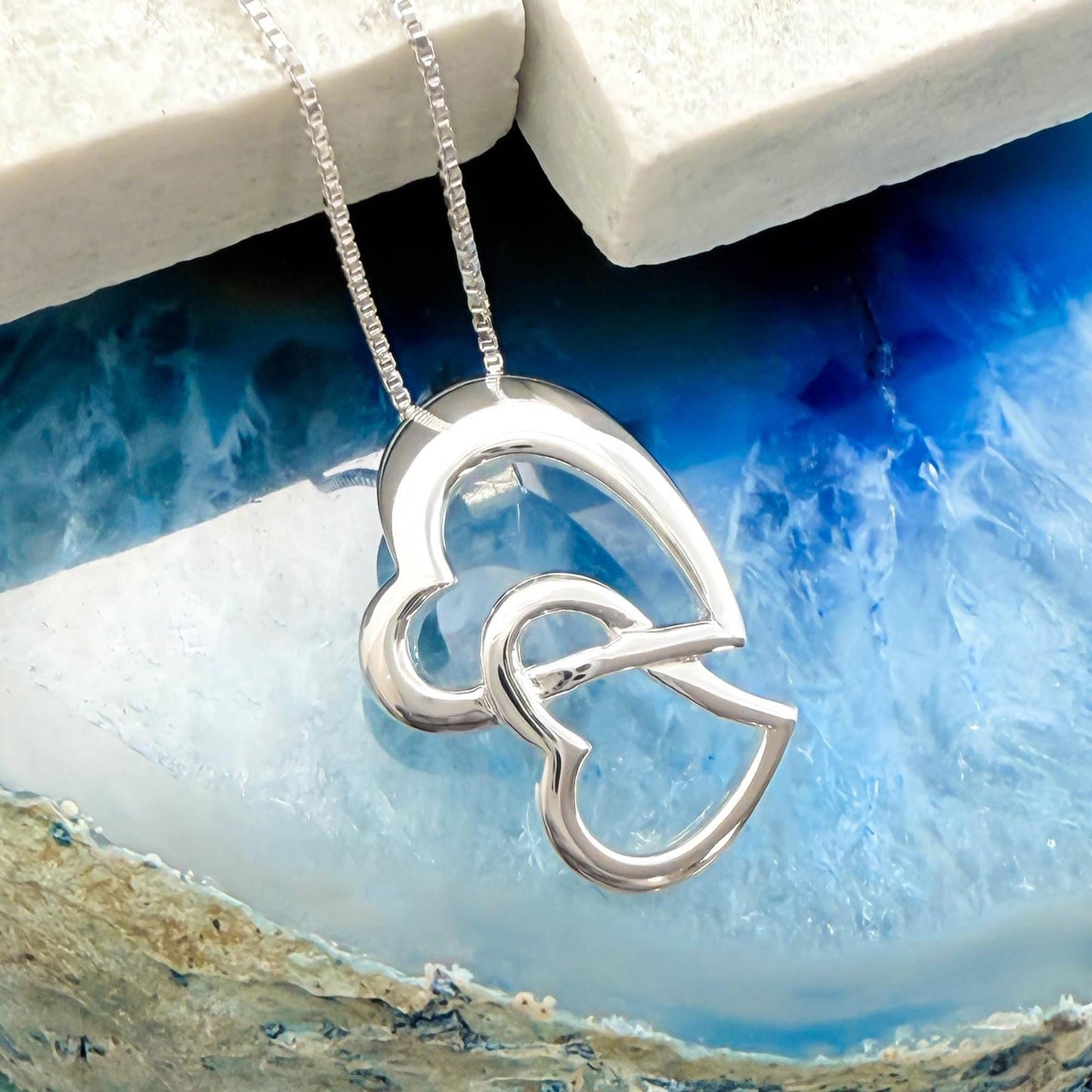 A silver heart-shaped pendant necklace is displayed against a blue and white background.