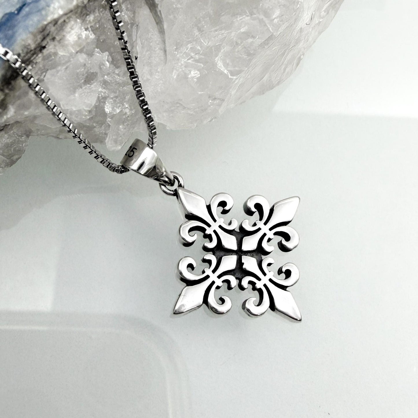 A silver pendant with an intricate, symmetrical design is displayed against a white background.