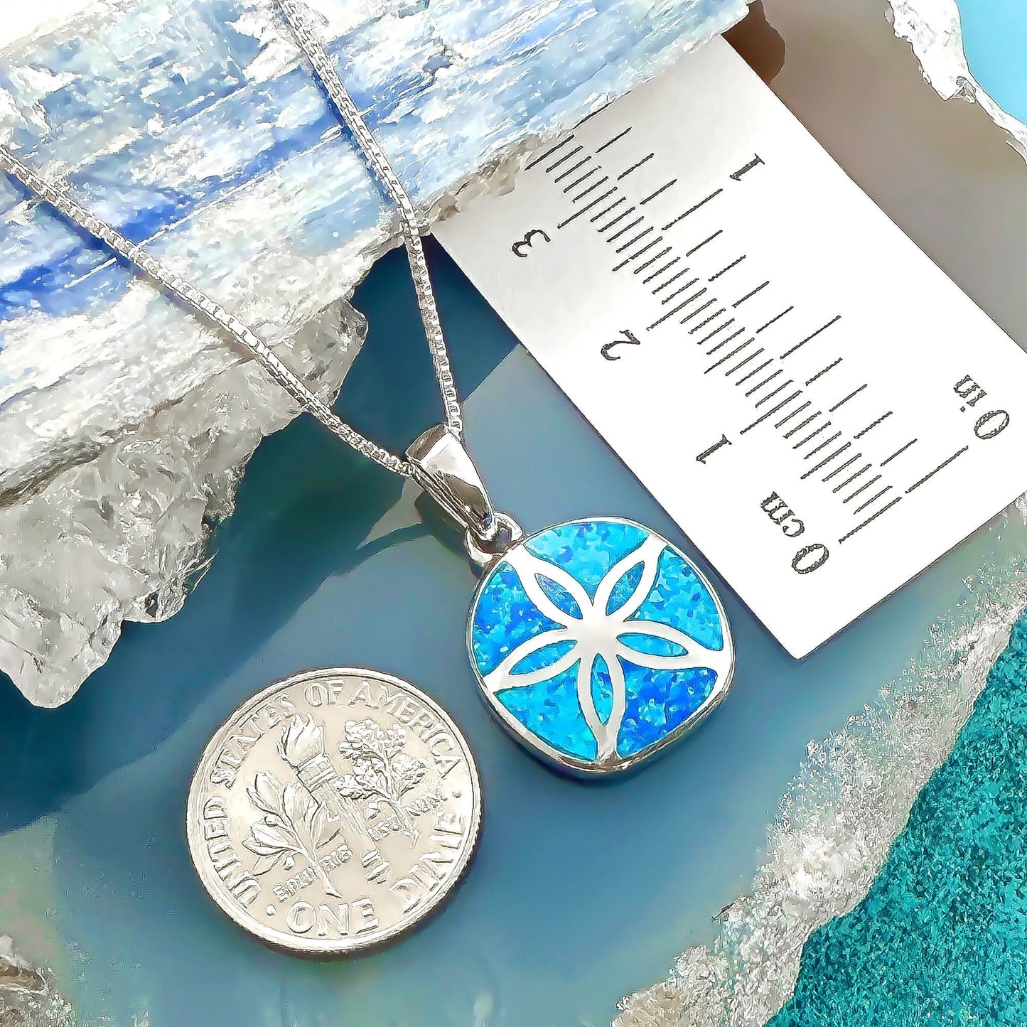 a silver necklace with a pendant and a United States one dollar coin placed on a blue and white surface.