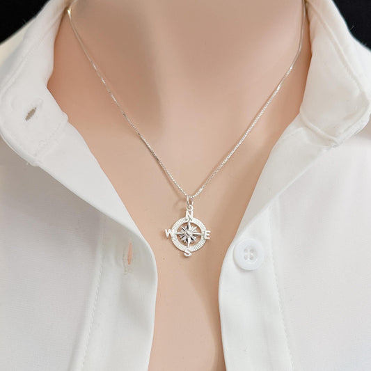 A silver necklace with a compass pendant is worn around a person's neck.