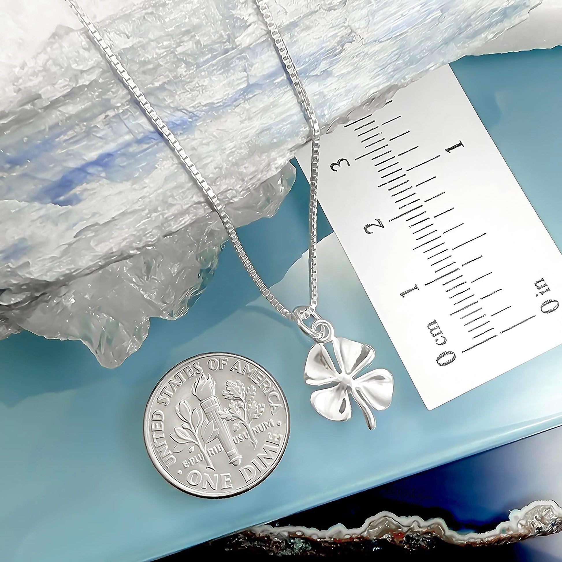 a silver necklace with a pendant, a United States one dollar coin, and a ruler for size comparison.