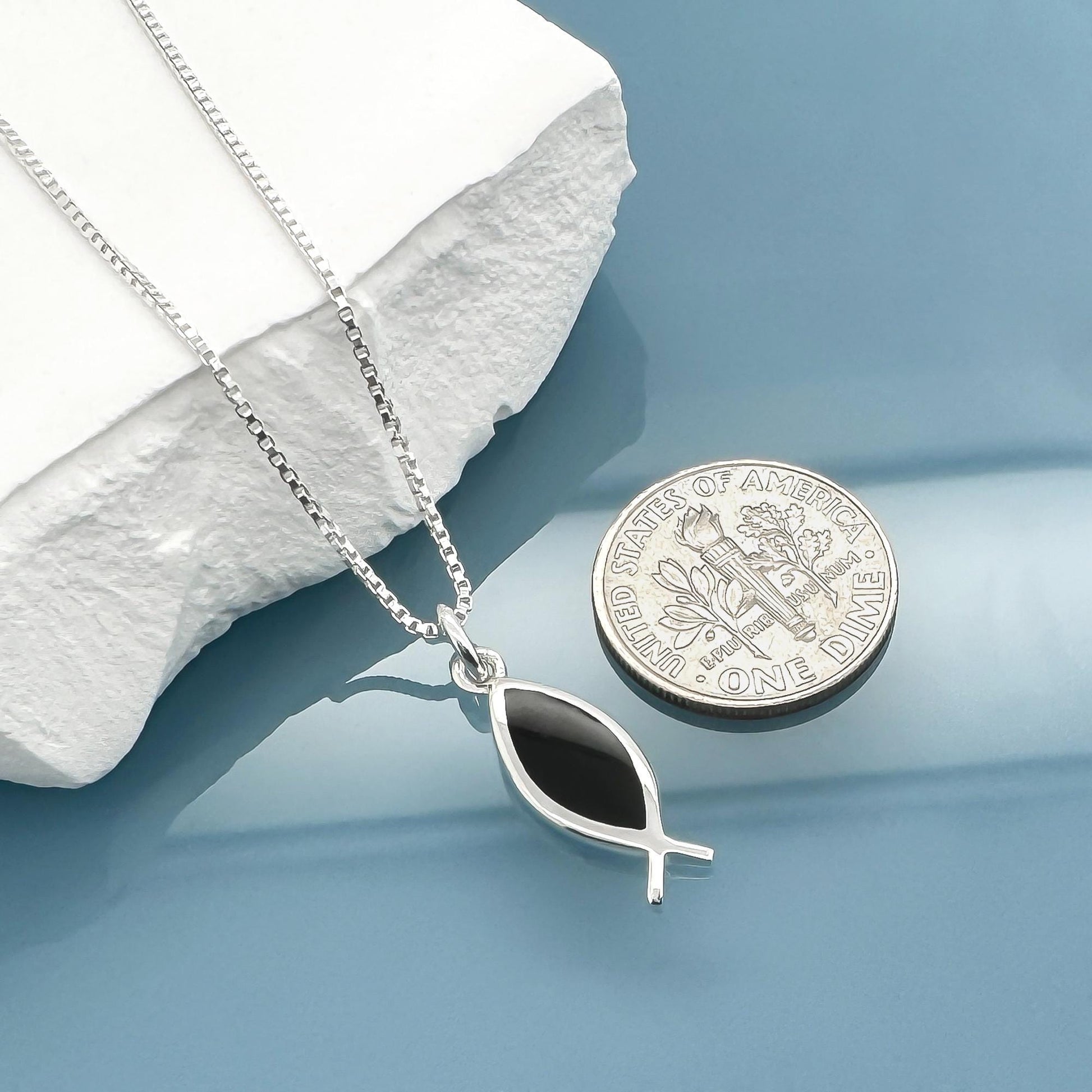 A silver necklace with a pendant and a silver coin are placed on a white surface.