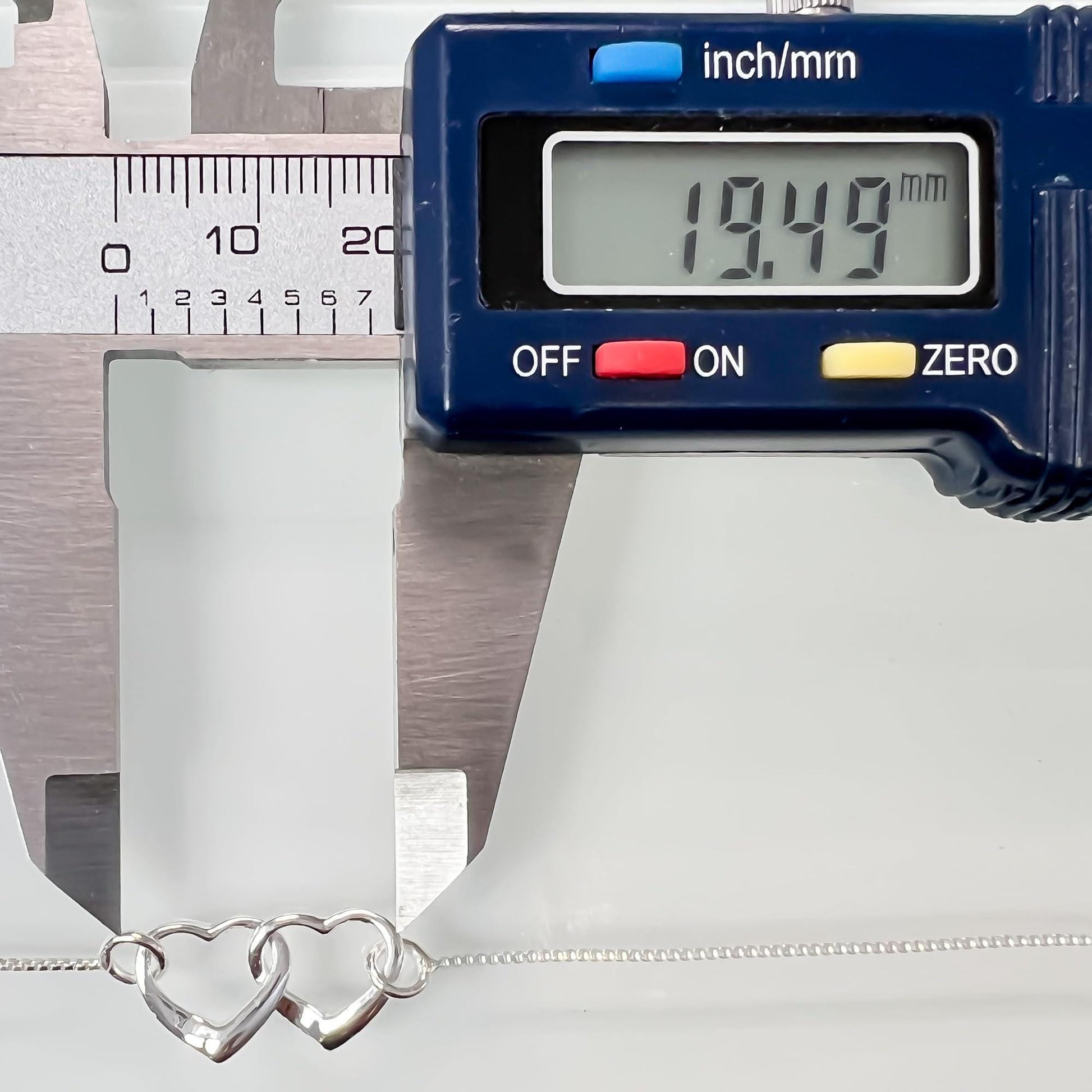 A digital caliper is measuring the length of a silver necklace chain, displaying the measurement as 19.49 millimeters.
