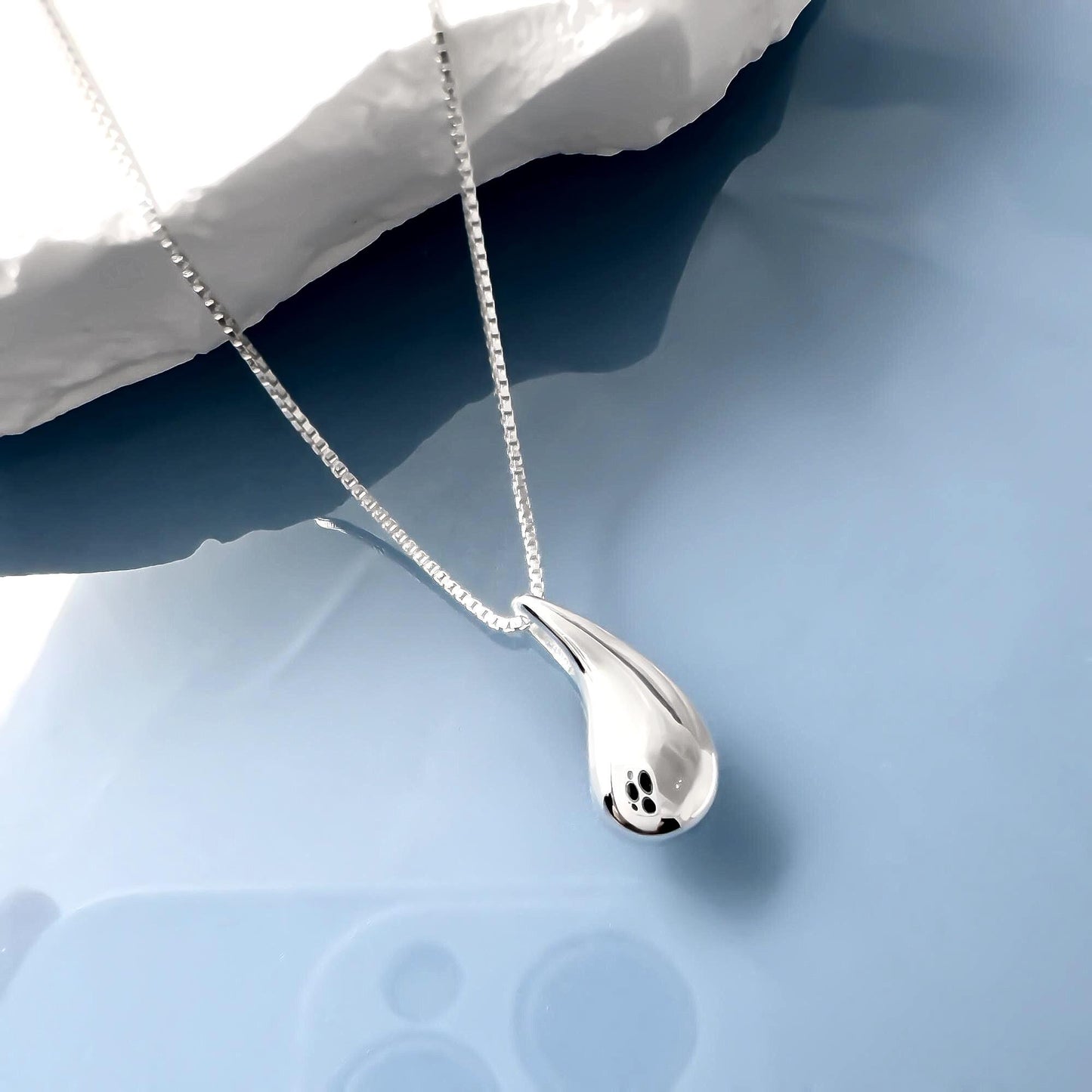 A silver necklace with a pendant is shown against a blue background.