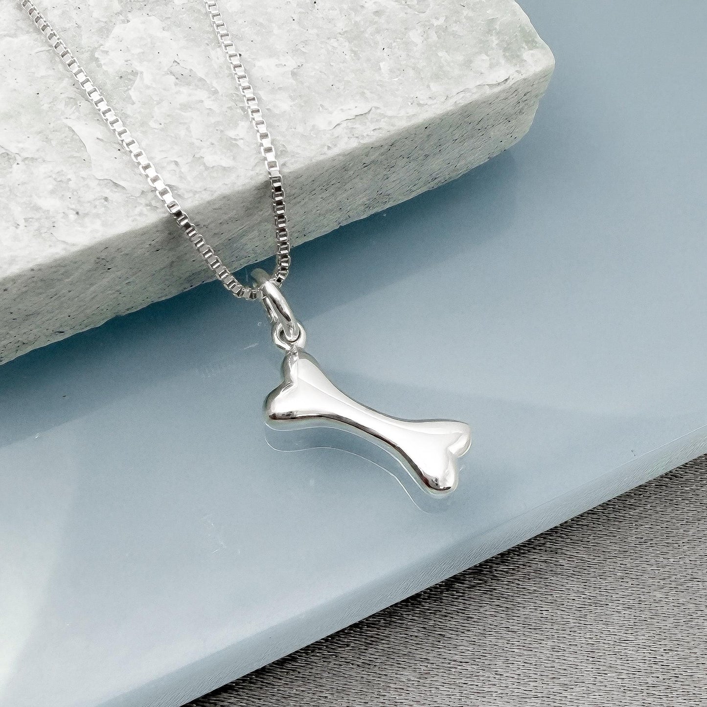 A silver-colored bone pendant is hanging from a silver chain, resting on a gray surface.
