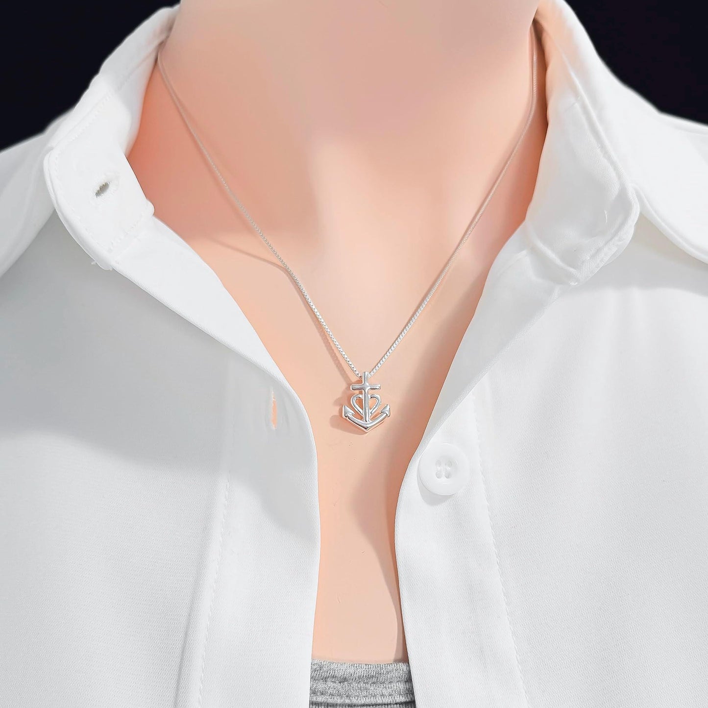 A close-up view of a person wearing a white collared shirt and a silver necklace with a small anchor pendant.