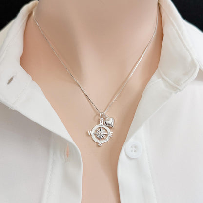 A silver necklace with a compass pendant is shown on a person wearing a white collared shirt.