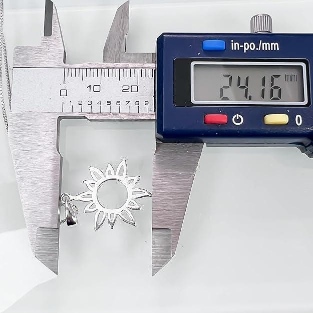 A digital caliper is measuring the size of a silver pendant with a flower design.