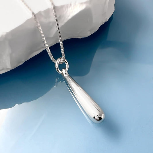 A silver necklace with a pendant is displayed against a blue background.