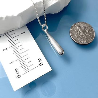 a silver pendant necklace with a small silver coin placed next to it on a blue surface.