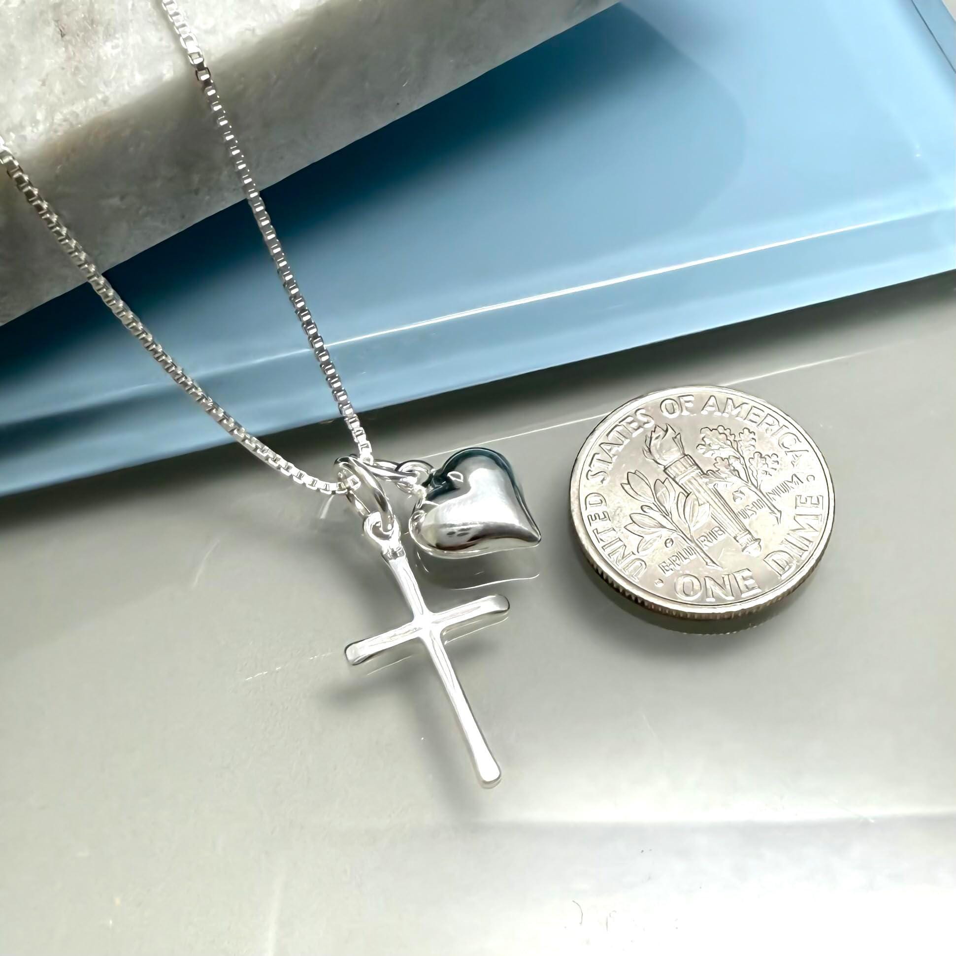 A silver cross necklace with a heart pendant is placed next to a United States one dollar coin.