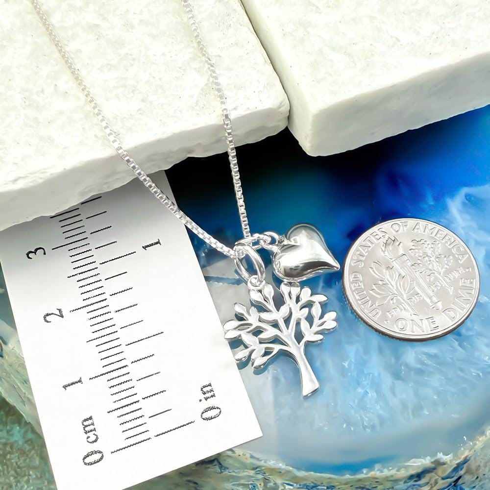 A silver necklace with a heart-shaped charm and a tree-shaped charm is displayed next to a U.S. quarter coin.