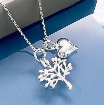 A silver necklace with a pendant featuring a tree design and a heart charm is displayed on a blue surface.