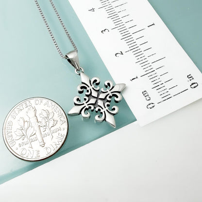 a silver pendant necklace with a decorative design, placed next to a United States one dollar coin for scale.