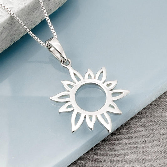 A silver pendant in the shape of a sun is displayed on a chain against a light blue background.