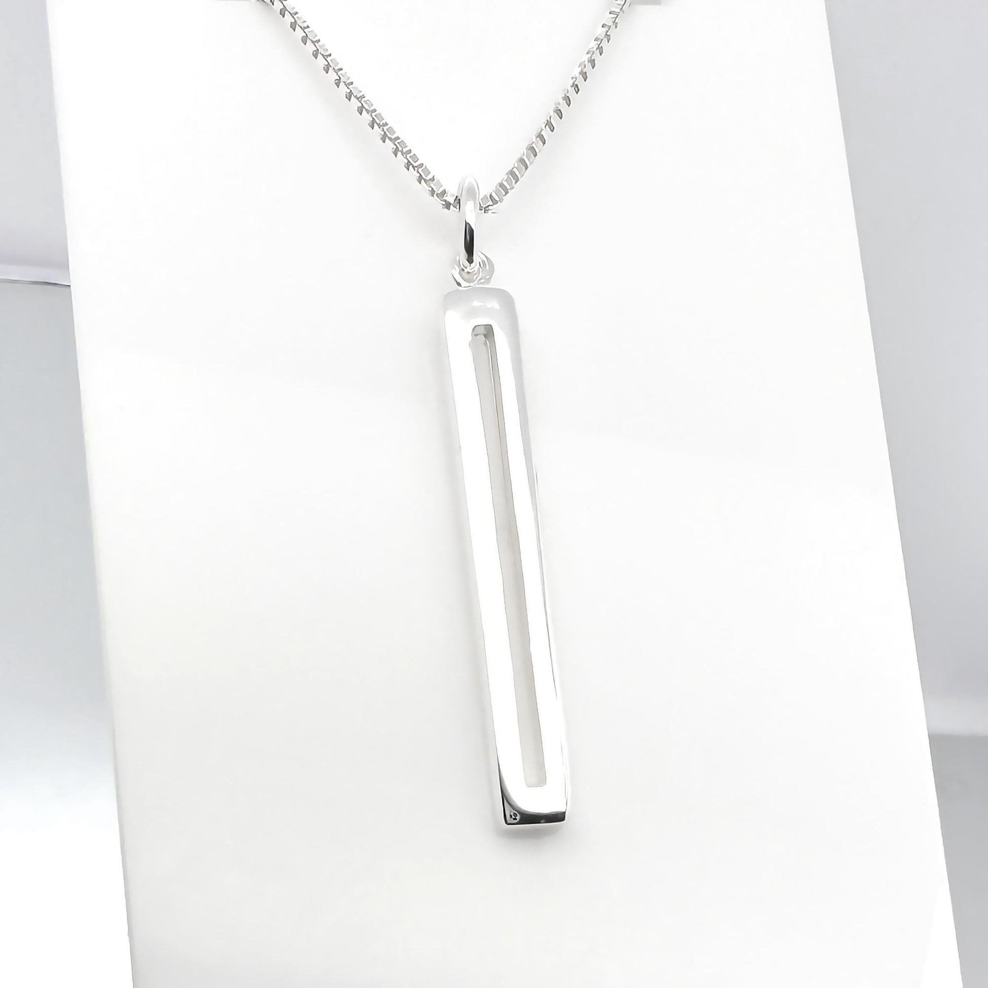 A silver necklace with a rectangular pendant is displayed against a white background.