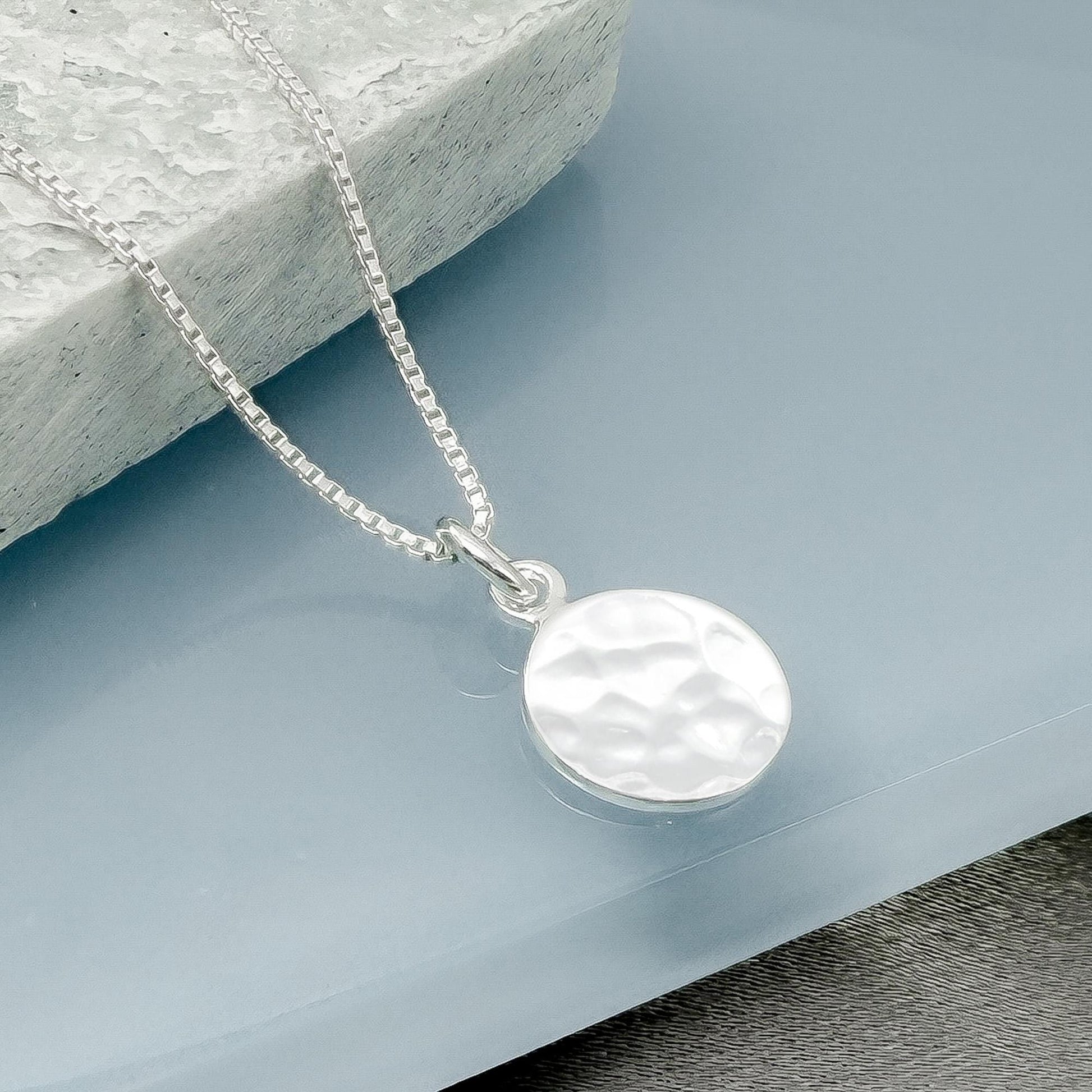 A silver necklace with a round pendant is displayed on a blue surface.