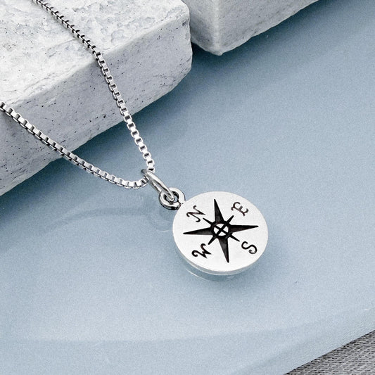 A silver necklace with a compass pendant is shown in the image.