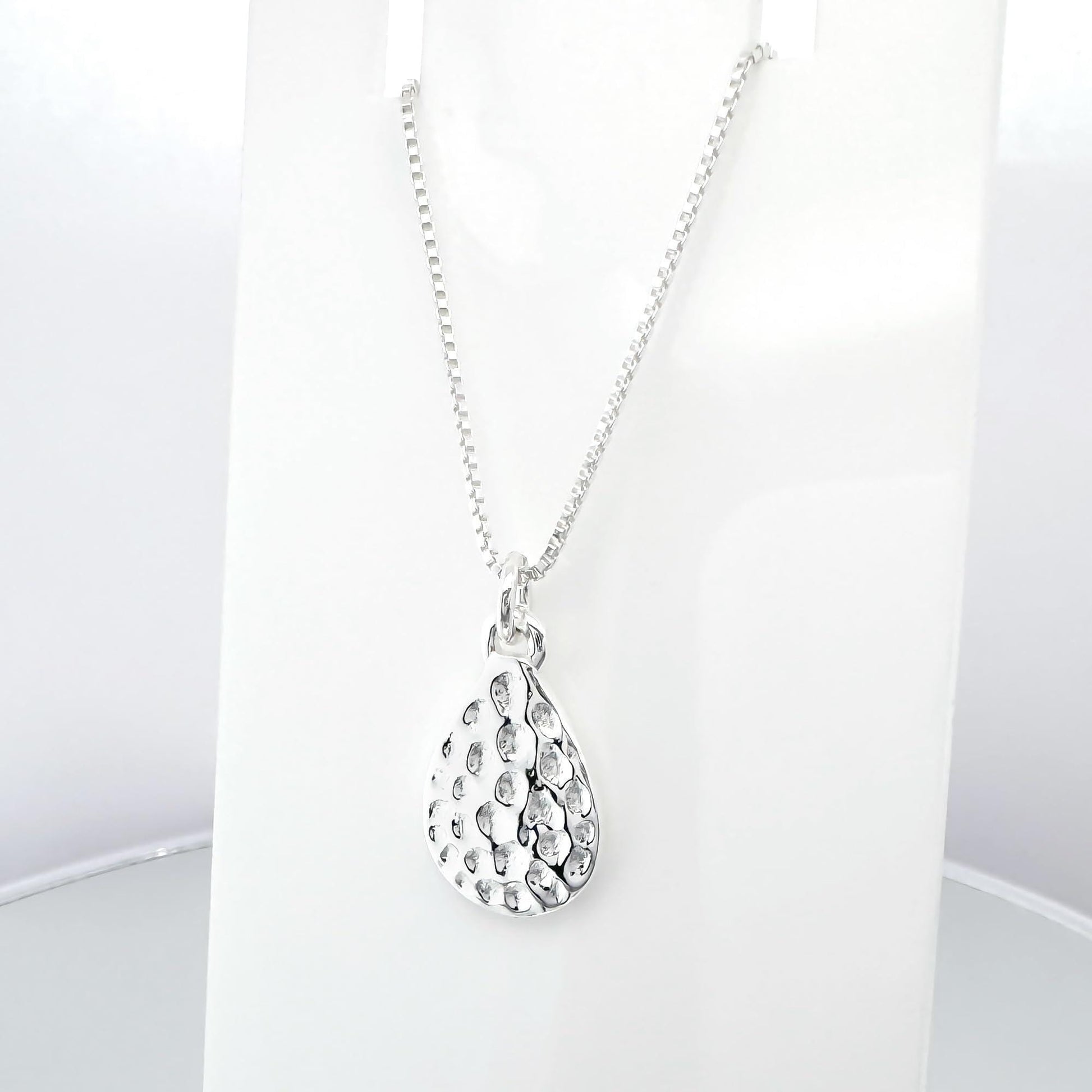 A silver necklace with a pendant featuring a pattern of small holes or dots.